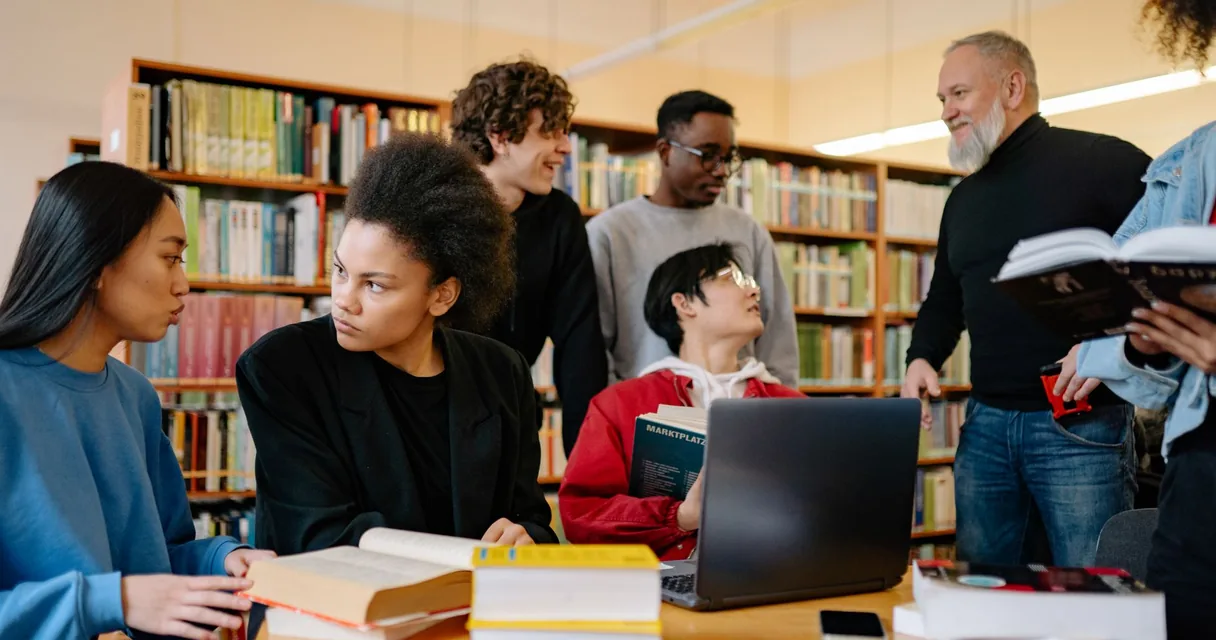 Estudantes universitários conversando em volta de livros e notebook numa biblioteca
