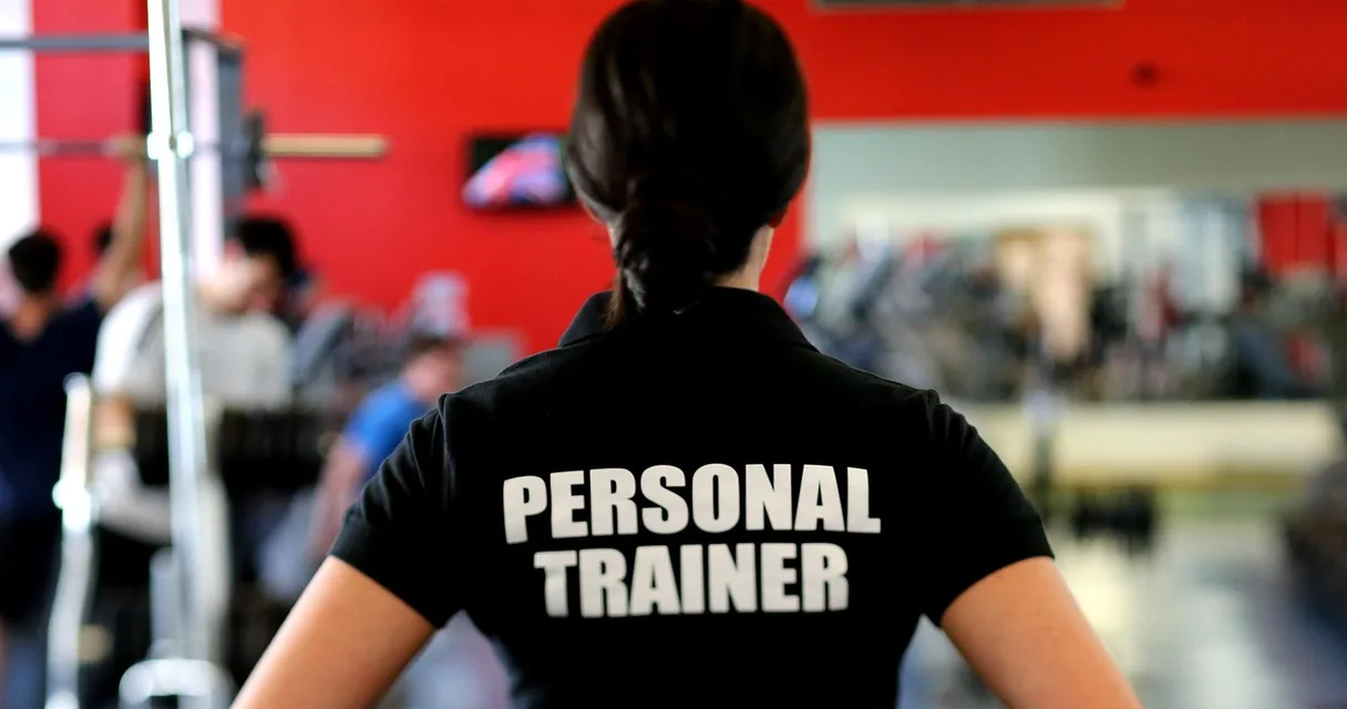 Personal trainer de costas, com camiseta identificada, observando alunos na academia