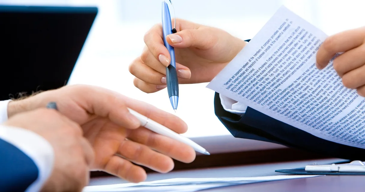 Mãos conferindo um documento impresso com caneta sobre a mesa