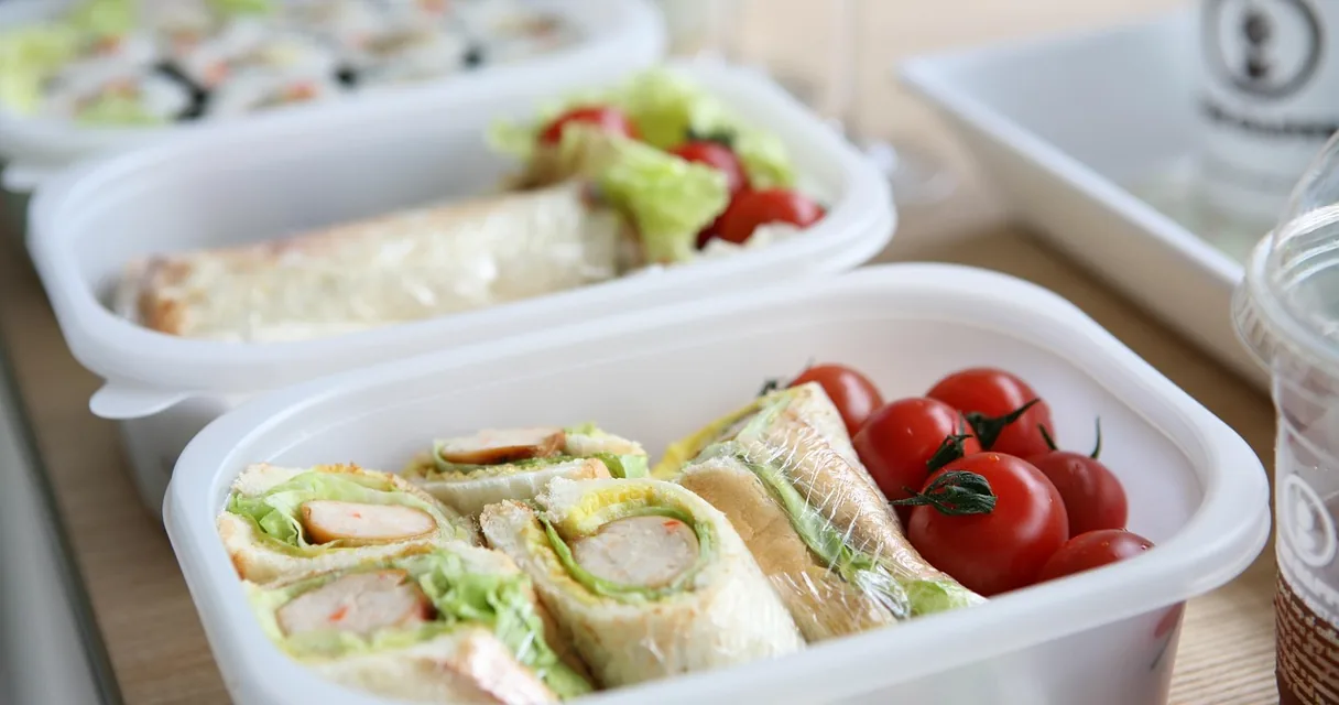 Marmitas de plástico com sanduíches e tomates em uma mesa